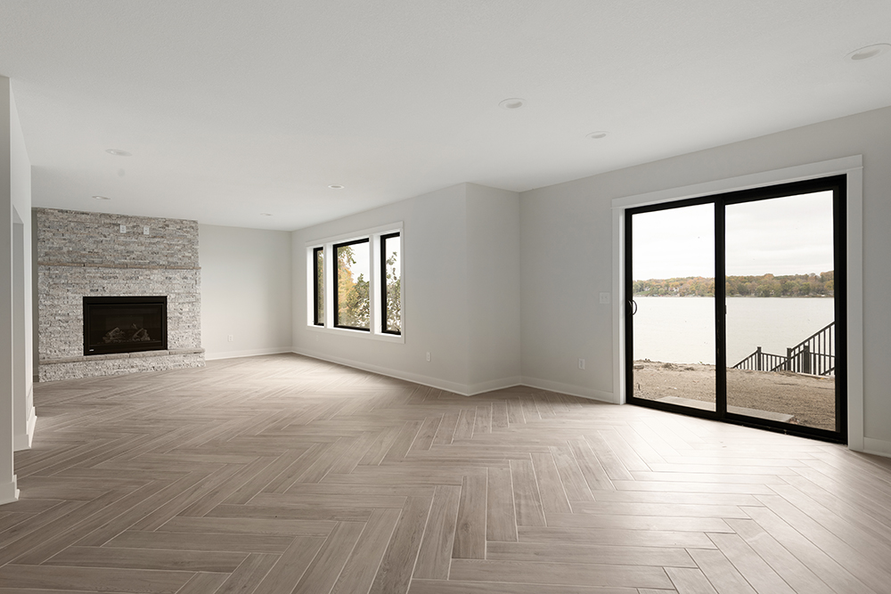 Empty living room with stone fireplace, herringbone tile floor, and lake view through sliding doors